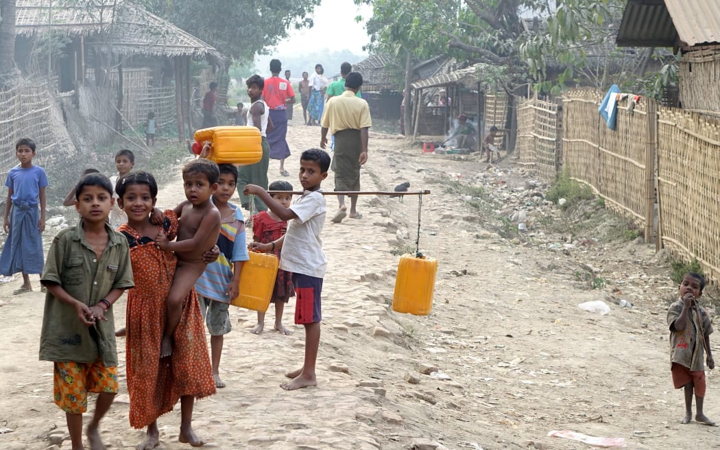 Children stand in mud and rock road carrying yellow plastic containers