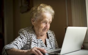 An elderly woman works on a laptop