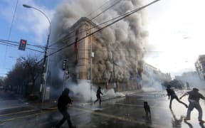 A security guard died when masked protestors burnt a pharmacy and supermarket.