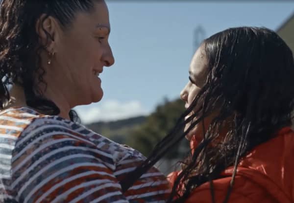 A woman in a t-shirt embraces a young girl with long curly hair.