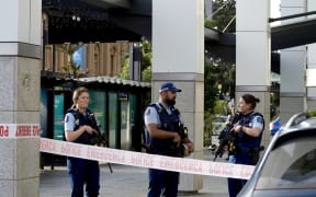 Armed police officers stand behind a cordon following a serious shooting incident in downtown Auckland on 20 July, 2023.