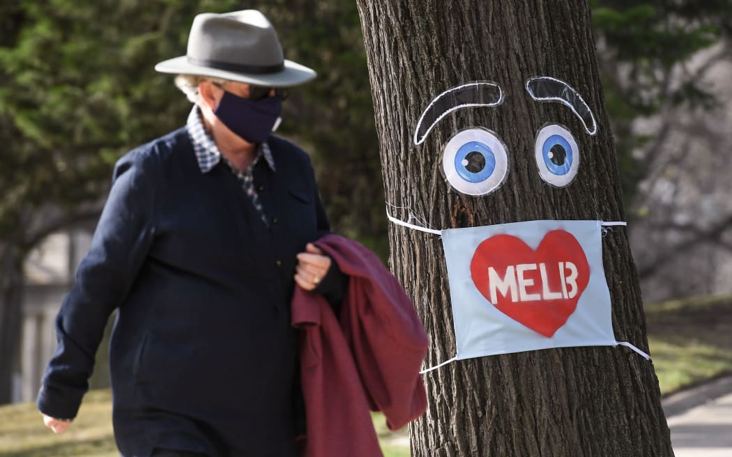 A man walks past a large face mask pinned to a tree in Melbourne on 3 August 2020 after the state announced new restrictions as the city battles fresh outbreaks of the Covid-19 coronavirus.
