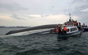 This handout photograph taken on July 19, 2025 and released by the Vietnam News Agency (VNA) shows relief personnel gathered around a capsized tourist boat (L) during a search and rescue operation in the Ha Long Bay, Quang Ninh province. At least 18 people have died and dozens remain missing after a tourist boat carrying more than 50 people capsized on July 19, in Vietnam's Ha Long Bay, state media said. (Photo by Vietnam News Agency / AFP) / RESTRICTED TO EDITORIAL USE - MANDATORY CREDIT "AFP PHOTO /  VIETNAM NEWS AGENCY (VNA) / - " - HANDOUT - NO MARKETING NO ADVERTISING CAMPAIGNS - DISTRIBUTED AS A SERVICE TO CLIENTS