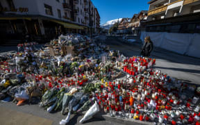 People gather around a makeshift memorial to pay their respect by laying flowers, candles and messages near the Constellation bar in Crans-Montana on January 6, 2026, in honour of the victims of the fire that ripped through the venue in the luxury Alpine ski resort on New Year's Eve.
