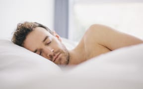 Young man lying on side asleep in bed (Photo by Kevin C Moore / Cultura Creative / Cultura Creative via AFP)