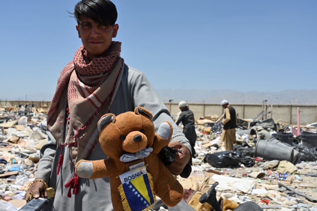 A man holds a teddy bear as people look for useable items at a junkyard near the Bagram Air Base in Bagram.