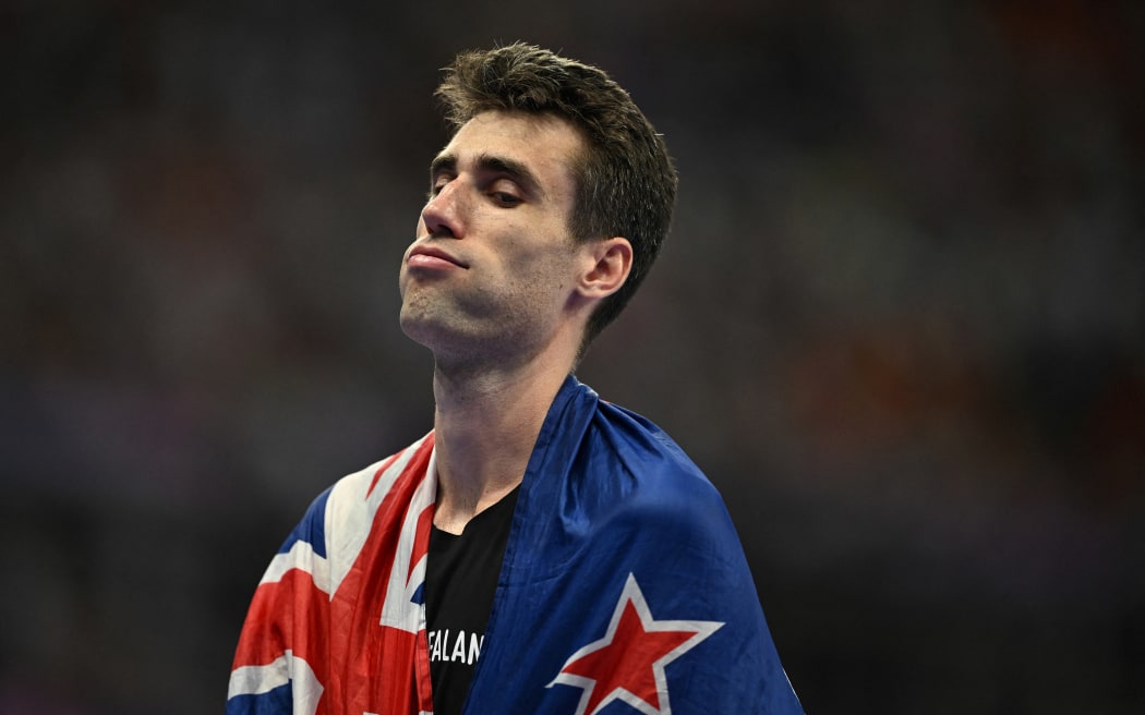 Hamish Kerr stands with a New Zealand flag draped around his shoulders.