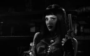 a black and white shot of Jessica Alba holding a gun and a liquor bottle.