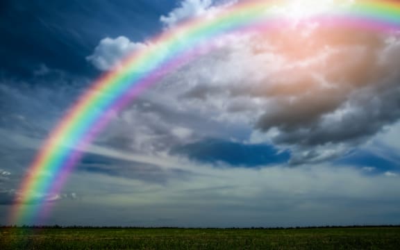 Picturesque view of green meadow and beautiful rainbow in cloudy sky