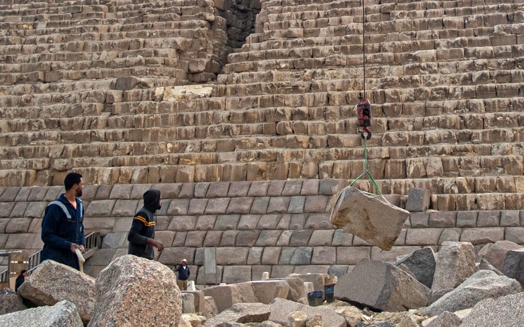 Workers watch as a stone is lifted by a crane during a conservation project by the base of the Pyramid of Menkaure (or Menkheres, built in the 26th century BC) at the Giza Pyramids Necropolis, west of Cairo, on January 29, 2024.