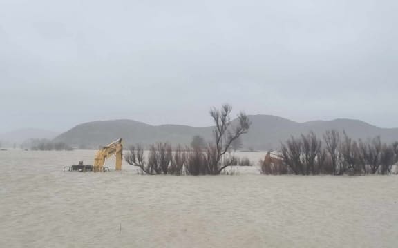 Heavy machinery caught in floodwater at the Wairoa River mouth on 26 June 2024. The digger is used to open up a channel in the bar to let floodwater escape more quickly.