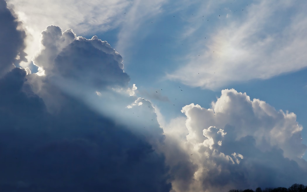 Dark and white clouds with shafts of sunlight and patches of blue sky.
