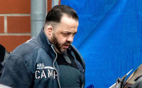 Niels Högel, accused of multiple murders and dressed in a bulletproof vest, is led to the prisoner transporter by judicial officers.