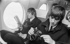 Beatles Ringo Starr and George Harrison on a plane with book and camera.