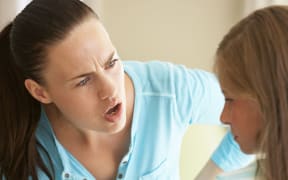 A close up image of an angry mother pointing her finger at her young daughter who looks chastened