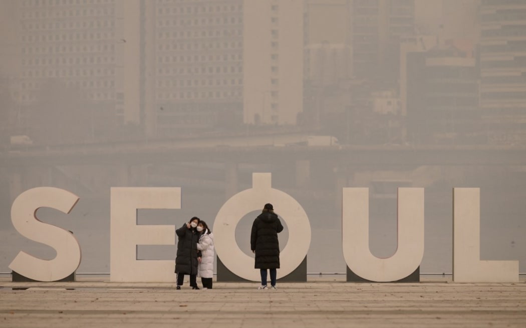 People wearing face masks take photos in front of the city skyline during heavily polluted weather conditions in Seoul on December 10, 2019. - According to the World Air Quality Index, levels of ultra-fine particuate matter reached 194 in South Korea.