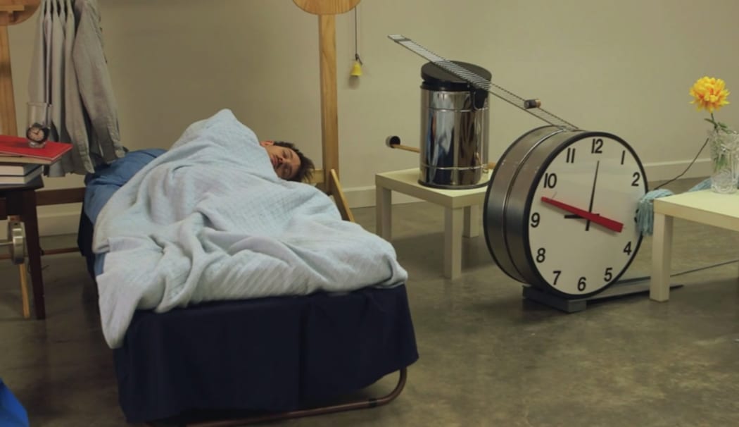 A still from the documentary, 'Joseph Gets Dressed' showing Joseph Herscher lying in bed surrounded by the machine that will wake him and dress him.