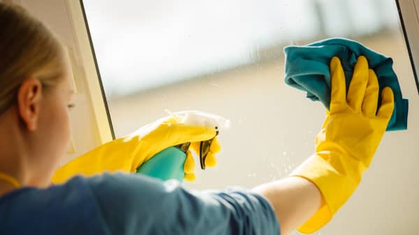 Young woman in yellow gloves cleaning window with blue rag and spray detergent. Spring cleanup, housework concept