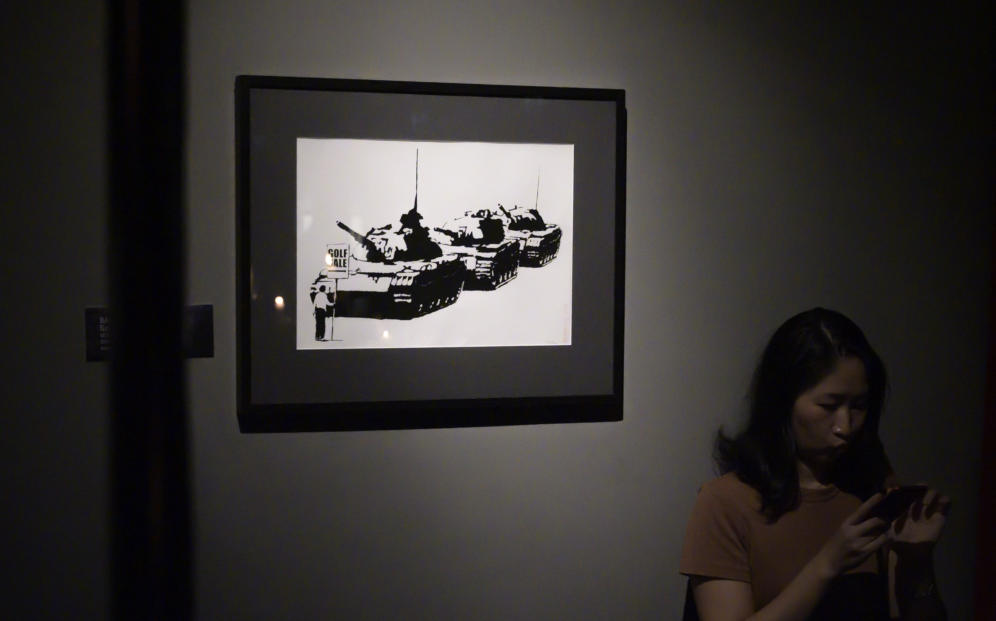 A woman uses her phones near "Golf Sale" by English street artist Banksy during an exhibition, "Street Art in Blu".