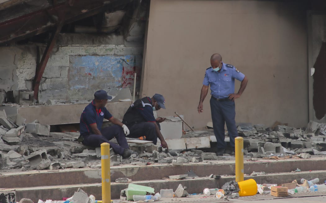 Police work at the site of a damaged building in Port Moresby on January 12, 2023. Troops patrolled the streets of Papua New Guinea's capital on January 12, under a state of emergency following riots that killed 16 across the country's two largest cities. (Photo by AFP)