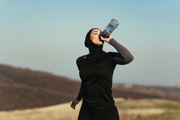 A female Muslim women drinking water from a bottle as she trains outdoors.