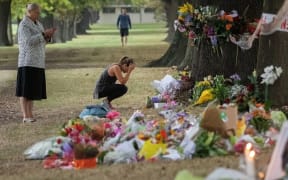 People stand next to floral tributes to those that were killed, across the road from the Al Noor mosque.