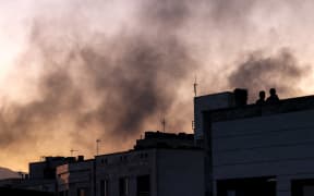 People stand on a rooftop amidst billowing smoke following an overinght Israeli strike in Tehran on June 17, 2025. (Photo by ATTA KENARE / AFP)
