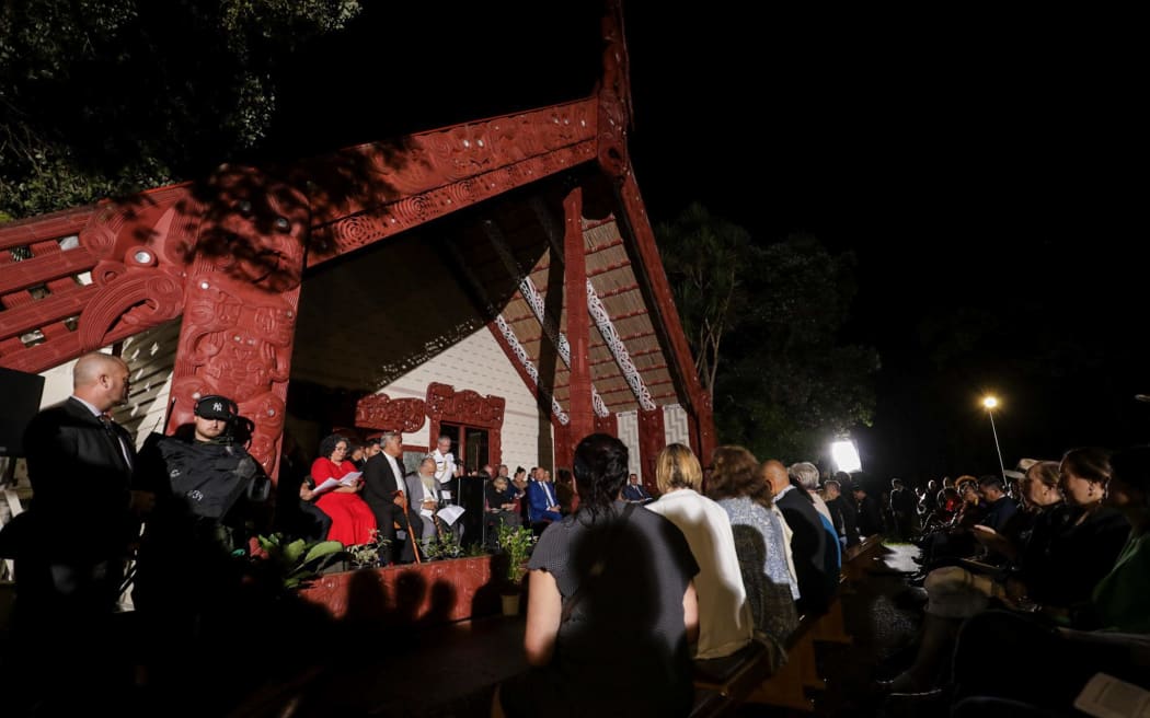 Te Whare Runanga is lit up as hundreds gather in the dark before it on the Waitangi Treaty Grounds.