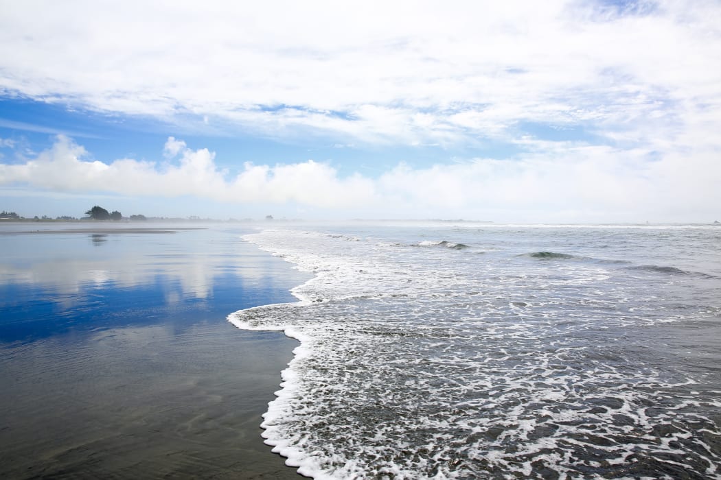 Coastline view on sky background in Westport of New Zealand. Soft waves splashing on sandy beach.