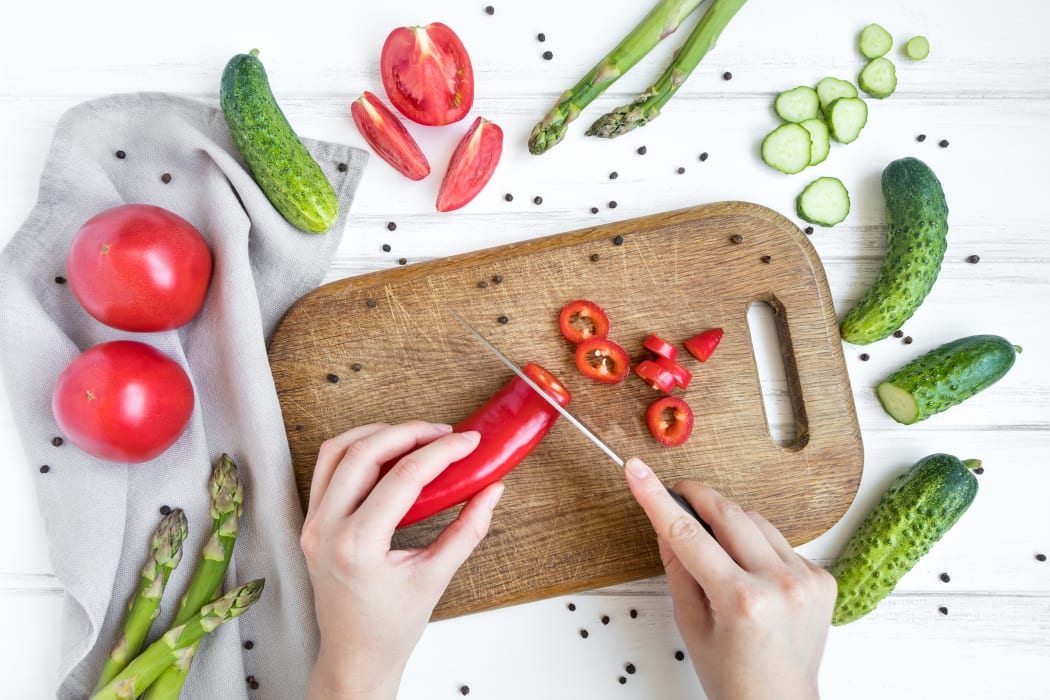 Woman hands slicing sweet pepper on wooden cutting board, surrounded by vegetables and eggs. Home cooking concept. Salad or any vegetarian dish. Flat lay, top view