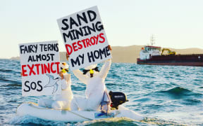 Pakiri seabed sand mining protestors voice their opposition as a McCallum Bros' sand mining ship moves by.