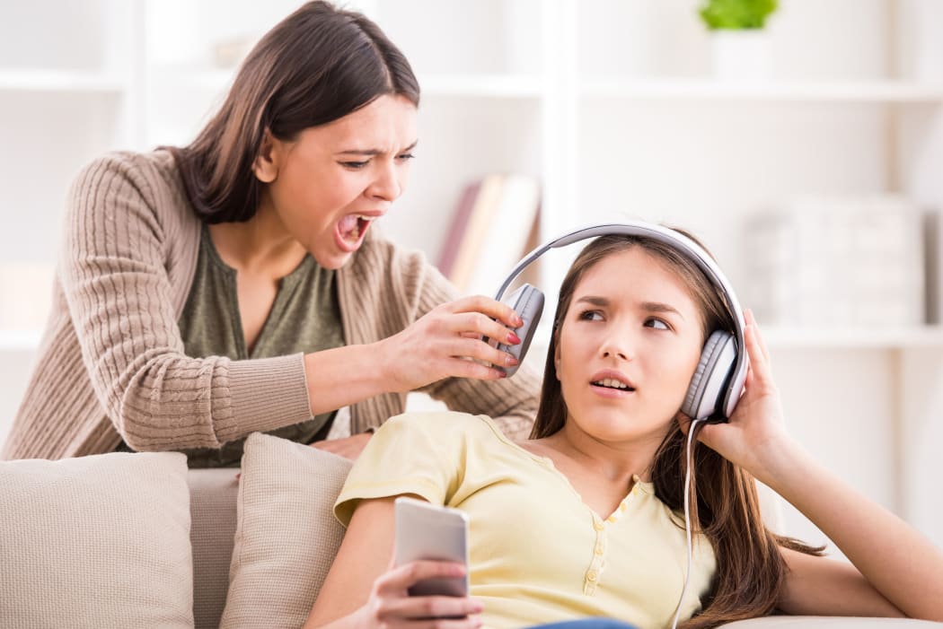 A photo of a mother pulling headphones off her teenage daughterwho is not listening to her