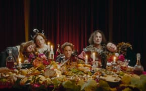 Still from the video to Soaked Oats' song 'Something'. The band and friends seated behind a sumptuous feast of food.