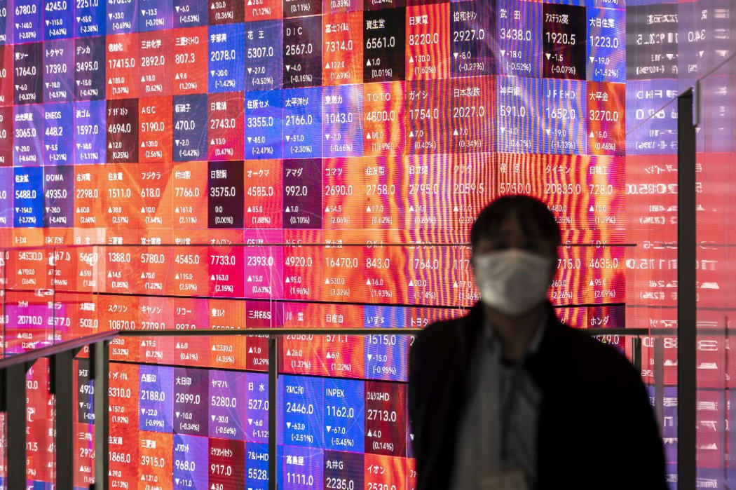 A man stands in front of an electronic share price board showing the numbers of the Tokyo Stock Exchange in Tokyo on February 25, 2022. (Photo by Charly TRIBALLEAU / AFP)