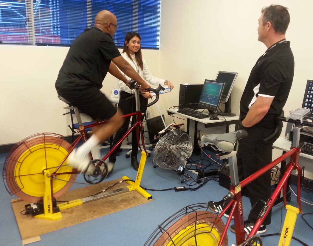 A photo of Ganesan Vadiveloo on the exercise bike with Shanggari Venugopal on the left and Kim Gaffney on the right