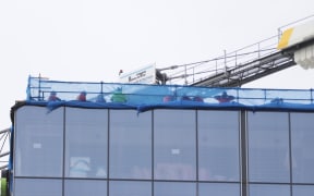 Construction workers can be seen at the top of a building at the centre of a serious shooting incident in downtown Auckland on 20 July, 2023.