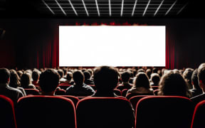 Cinema blank screen and people in red chairs in the cinema hall. Blurred People silhouettes watching movie performance.