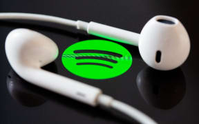 Headphones are on the screen of a smartphone, which displays the logo from the music streaming service Spotify.