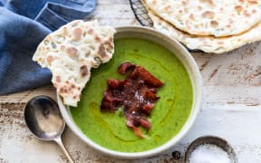 A bowl of bright green pea, spinach and tarragon soup garnished with crisp bacon and seedy yoghurt flatbreads.