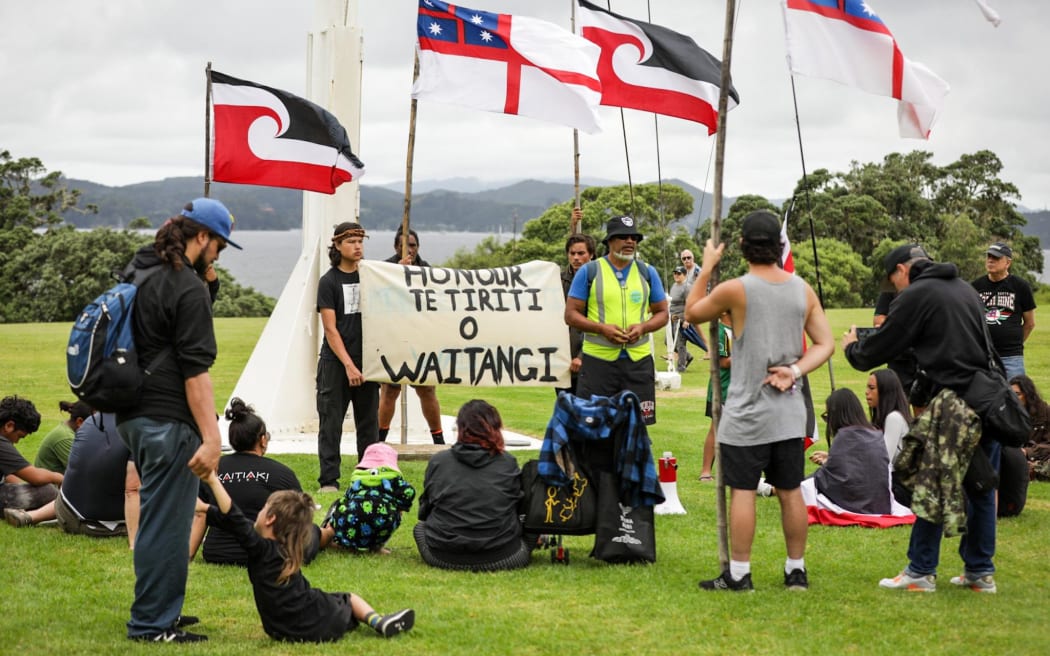 People holding a 'Honour Te Tiriti o Waitangi' sign at Waitangi.