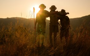 silhouette of male students standing and hugging each other in the grass on the mountain Boy Scouts rejoice at rock climbing success in the evening at sunset.