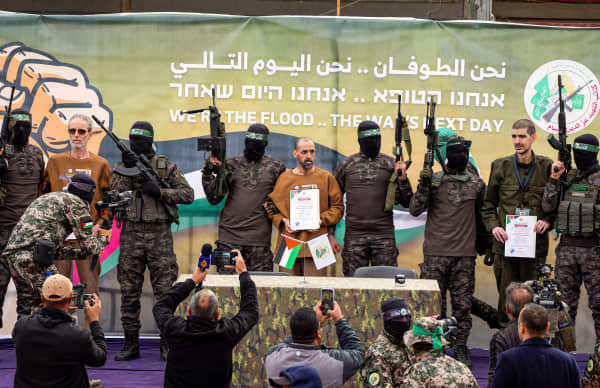 Palestinian Hamas fighters escort Israeli hostages (L-R) Ohad Ben Ami, Or Levy and Eli Sharabi on a stage before handing them over to a Red Cross team in Deir el-Balah, central Gaza, on 8 February 2025.