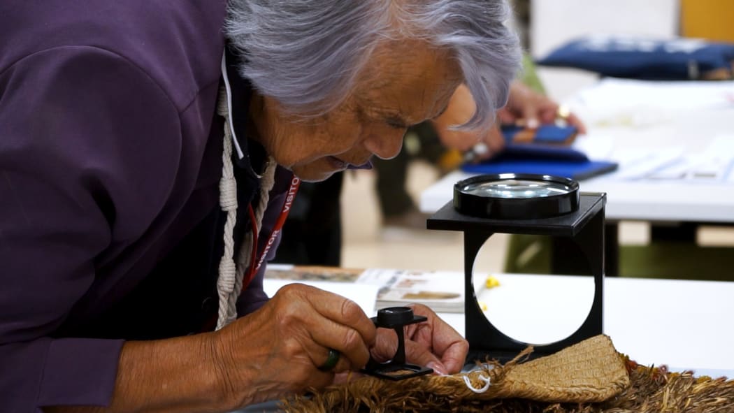 Matekino Lawless using a magnifying glass to view the close weave.