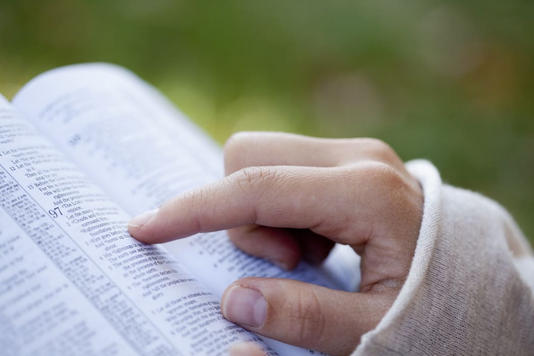 A file photos shows a woman's hand pointing to a Bible passage.