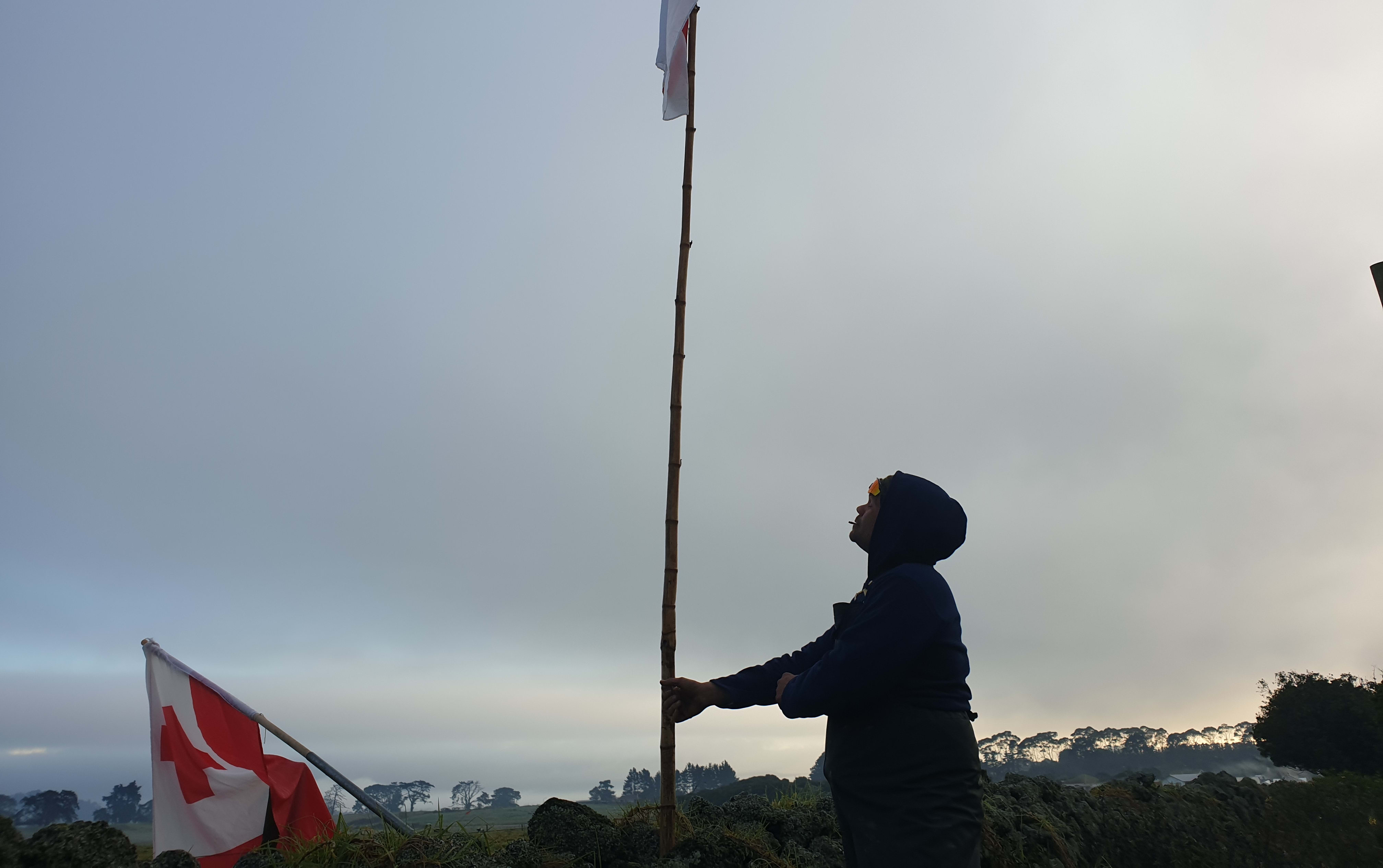 A person raising a flag at Ihumātao.