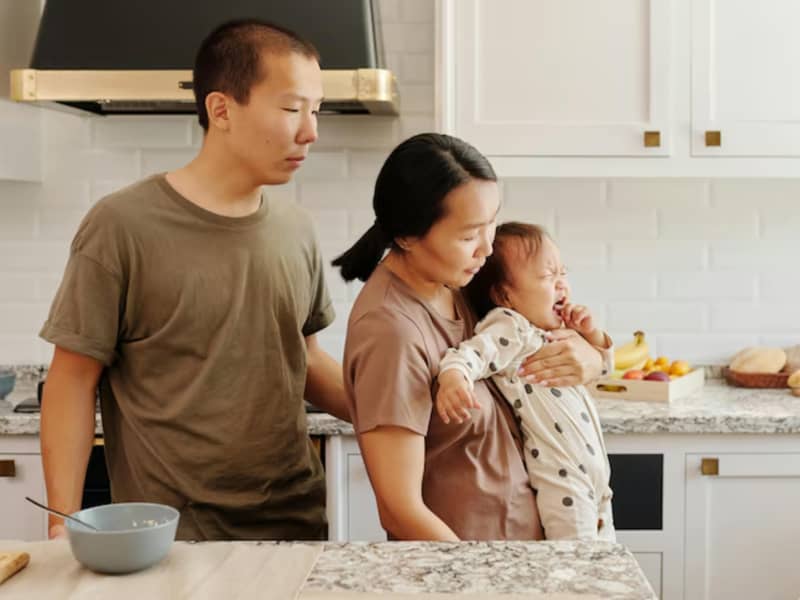 An Asisn woman holds a baby while the father looks on.