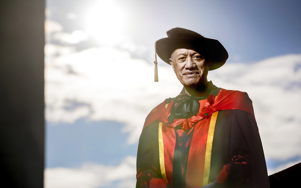 Te Piere smiles at the camera. He wears a graduate's robes and hat.