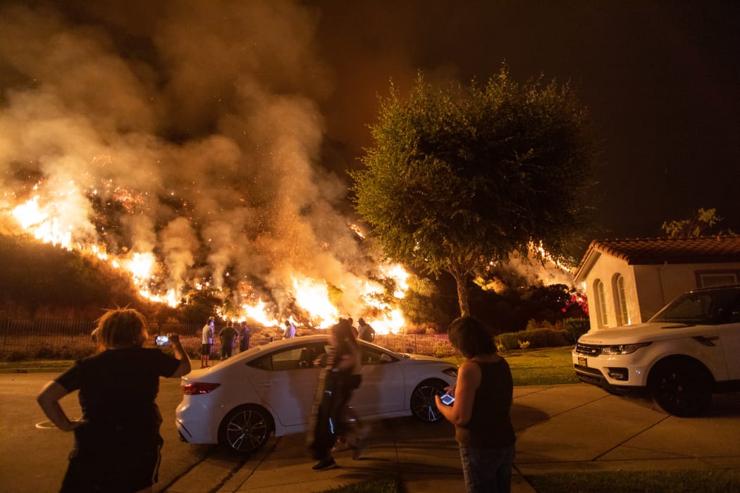 People stand next to flames rising from the Ranch fire in the San Gabriel mountains east of Los Angeles.