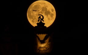 The full moon is pictured behind the Soviet symbol of hammer and sickle as a plane is silhouetted in Moscow late on 23 July, 2021.
