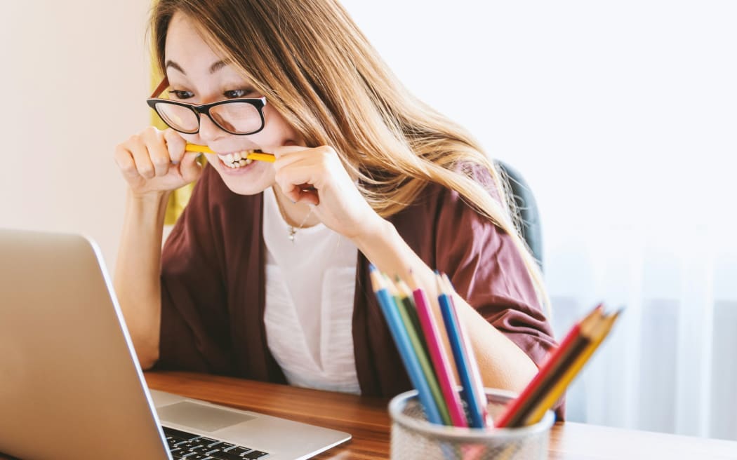 Confused and angry woman bites down on a pencil while looking at a laptop.